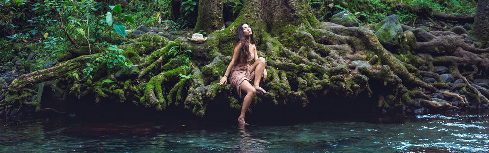 Women about to step into a flowing stream in Hawaii. She looks about to embark on a self-care routine.